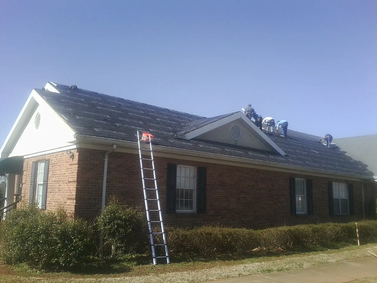 Crew tearing shingles off a brick ranch roof with a ladder set — Metal Roof Repair work by our crew in Floral City