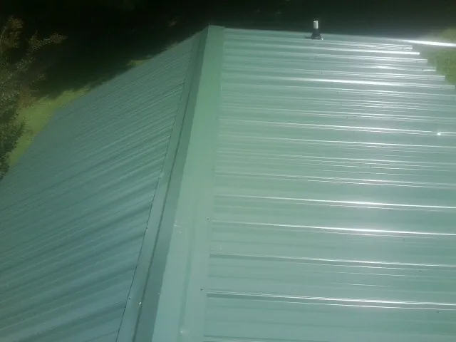 New green metal panels meeting at the ridge of a roof — Flat Roof Repair work by our crew in Floral City