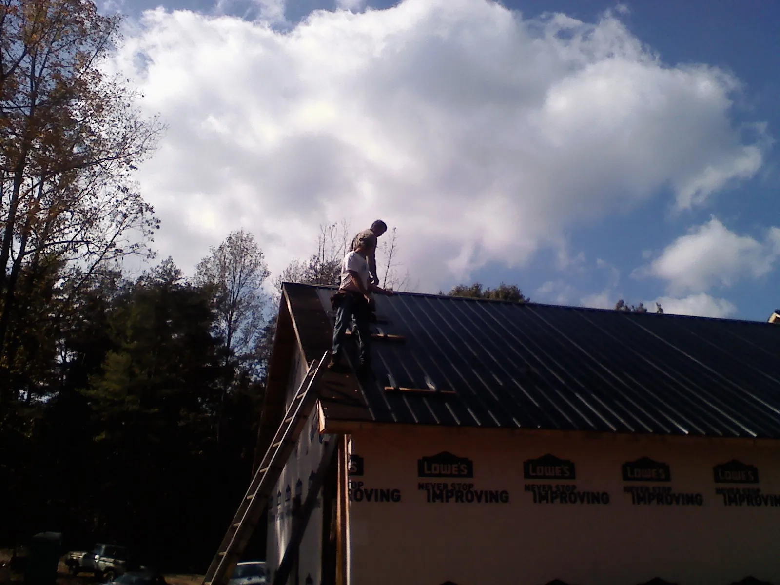 Roofer fastening dark metal panels high against a cloudy sky, from a Roof Inspection job in Floral City