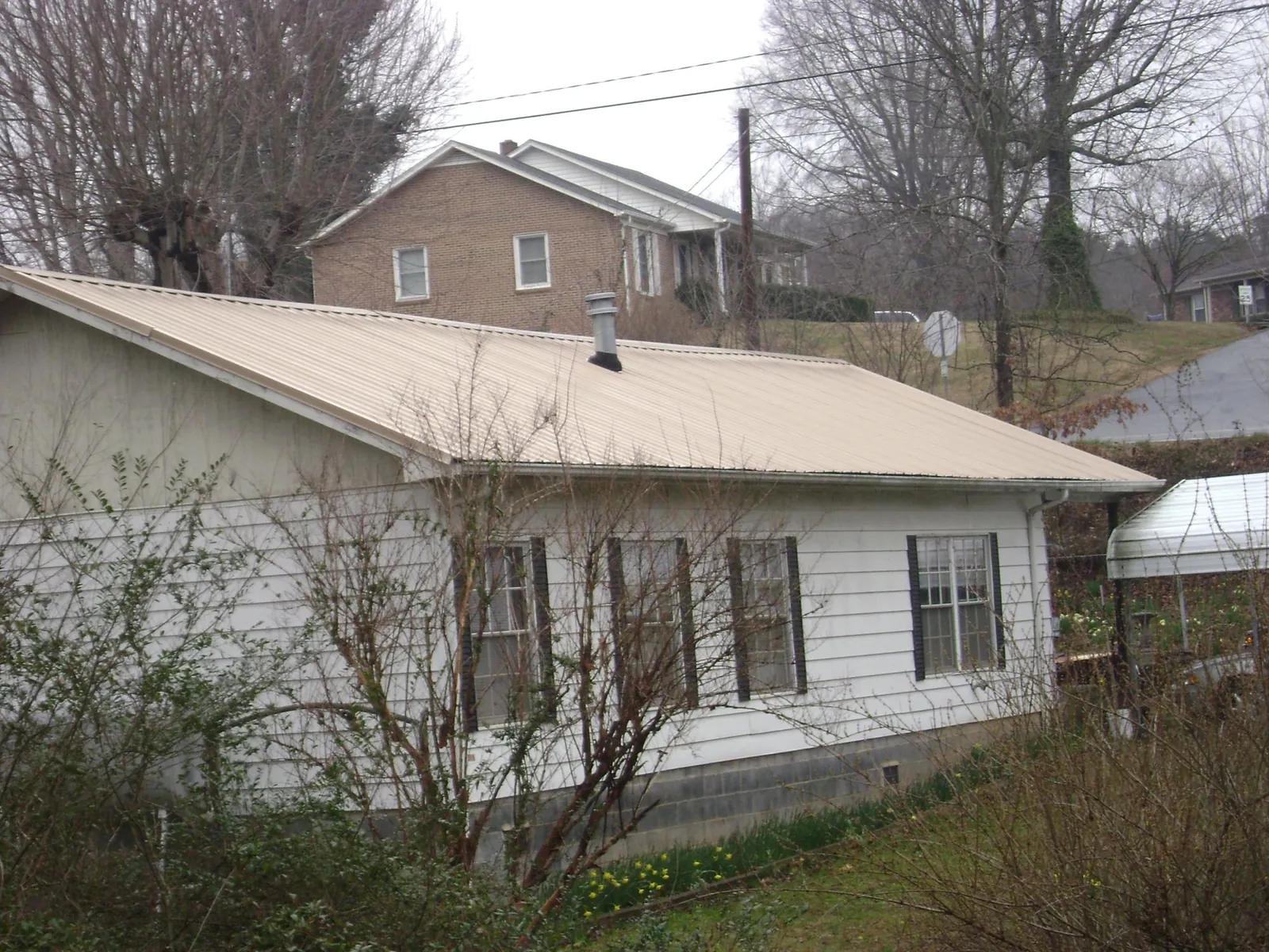 Tan metal roof on a white sided house set into a hillside — Commercial Roofing by Roofing Brothers in Floral City